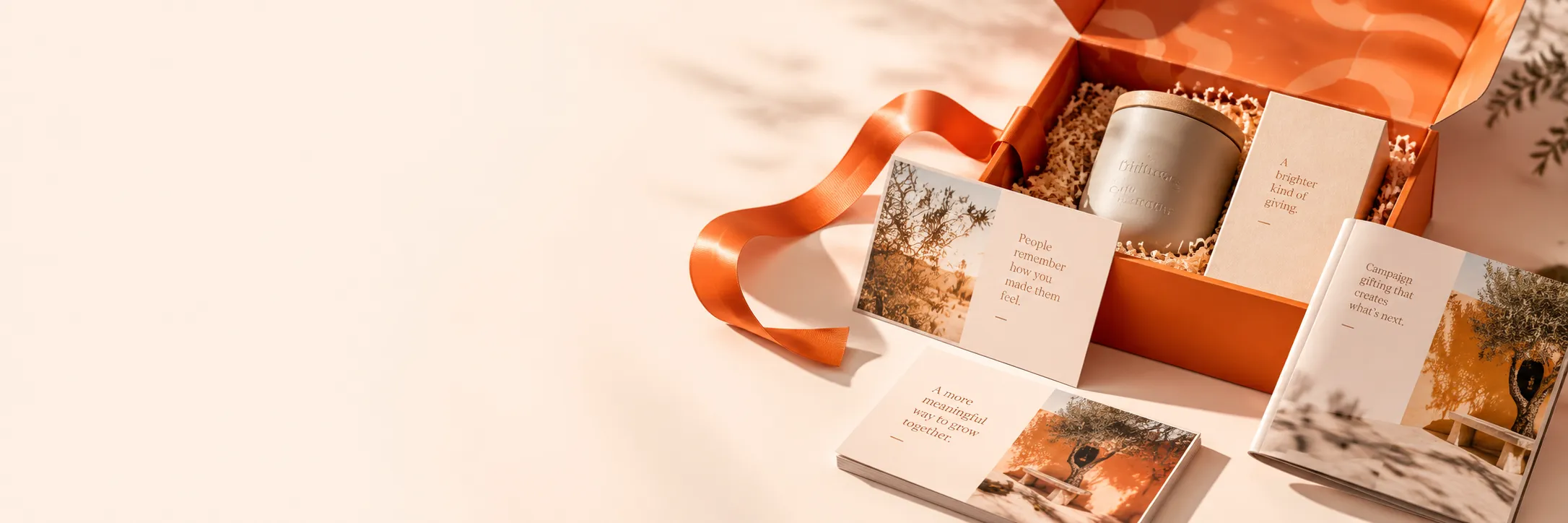 An orange gift box with a candle and illustrated message cards tied with orange ribbon