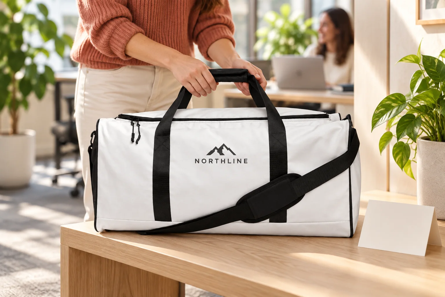 A new colleague in a terracotta jumper placing a white and black branded duffle bag on a bench in a bright office.